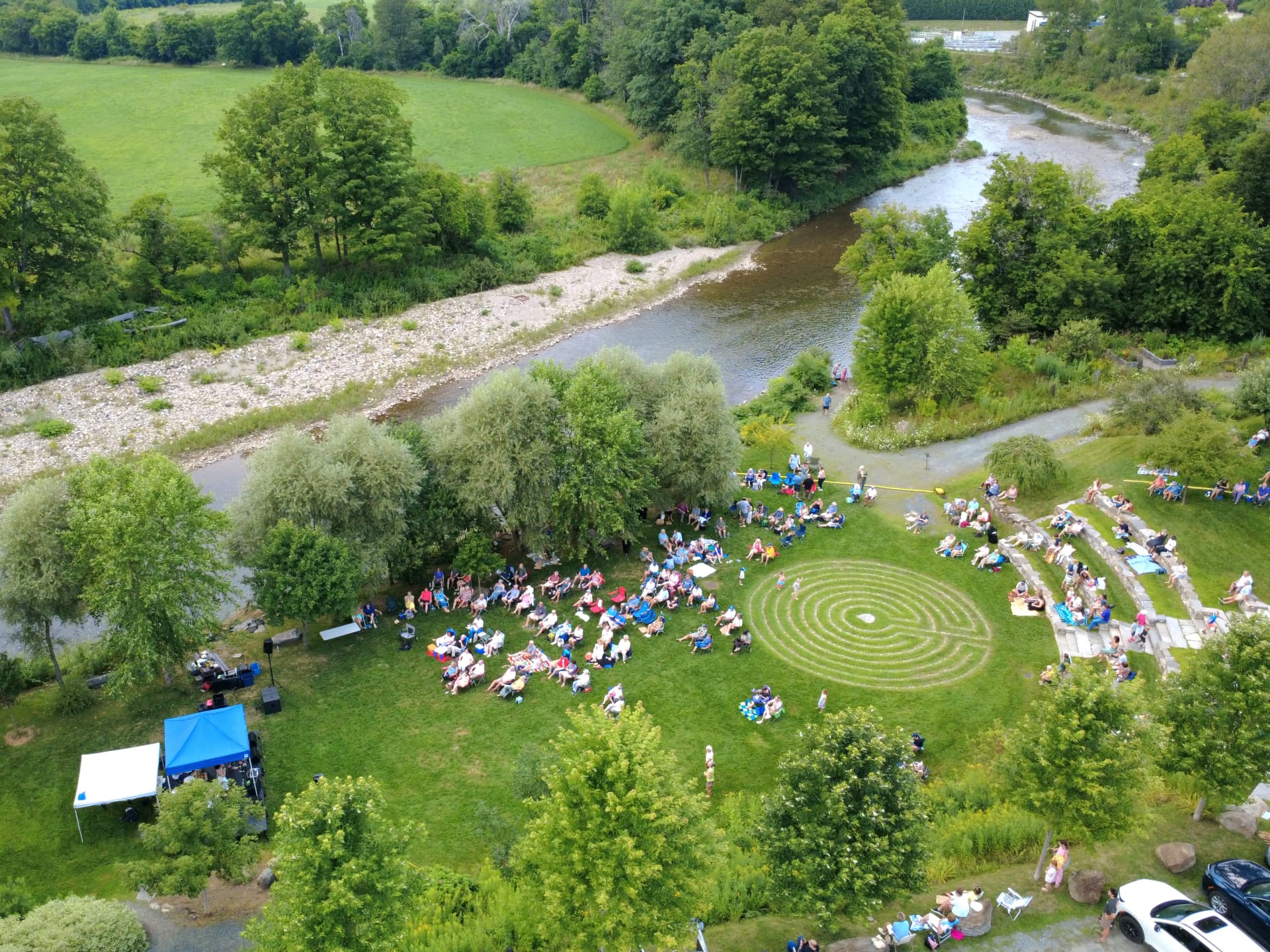 Aerial view of an audience gathered on a lawn beside the river at an outdoor community event