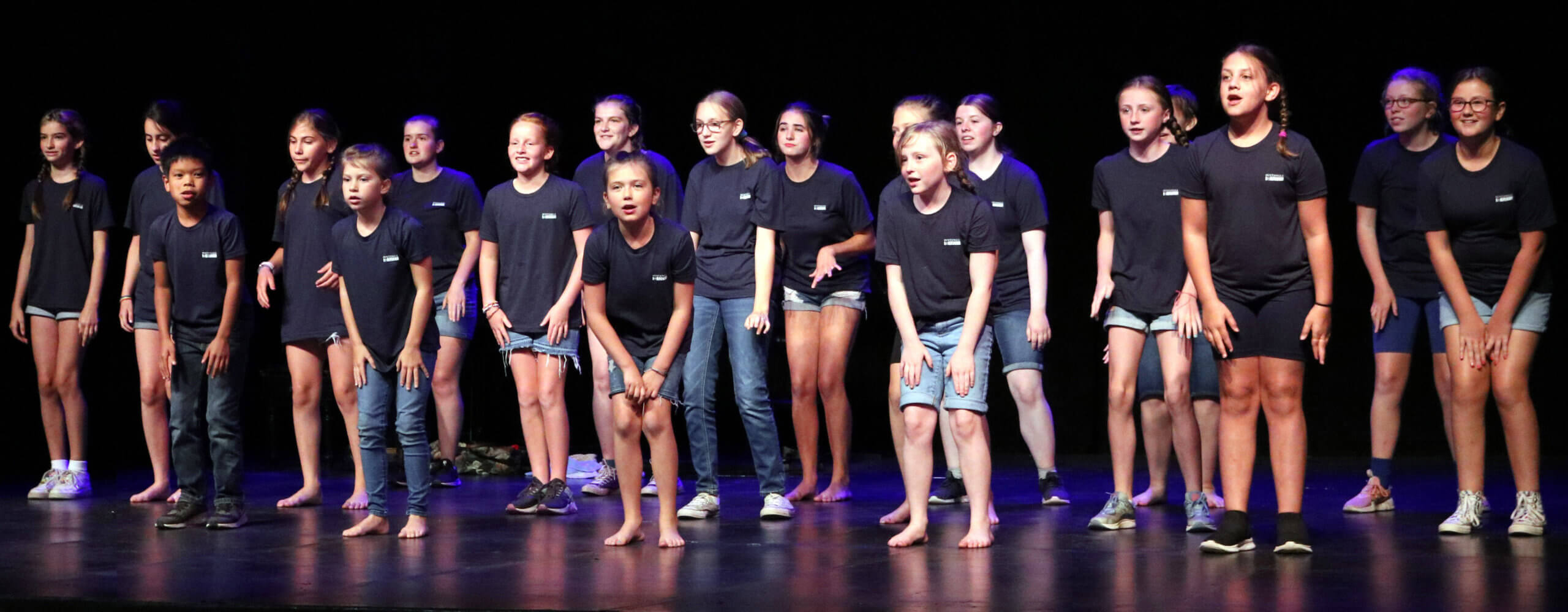 Young performers standing together onstage under warm theatre lights
