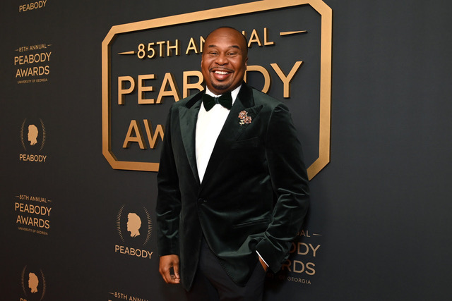 Roy Wood Jr. smiling in a black tuxedo on the red carpet at the 85th Annual Peabody Awards.