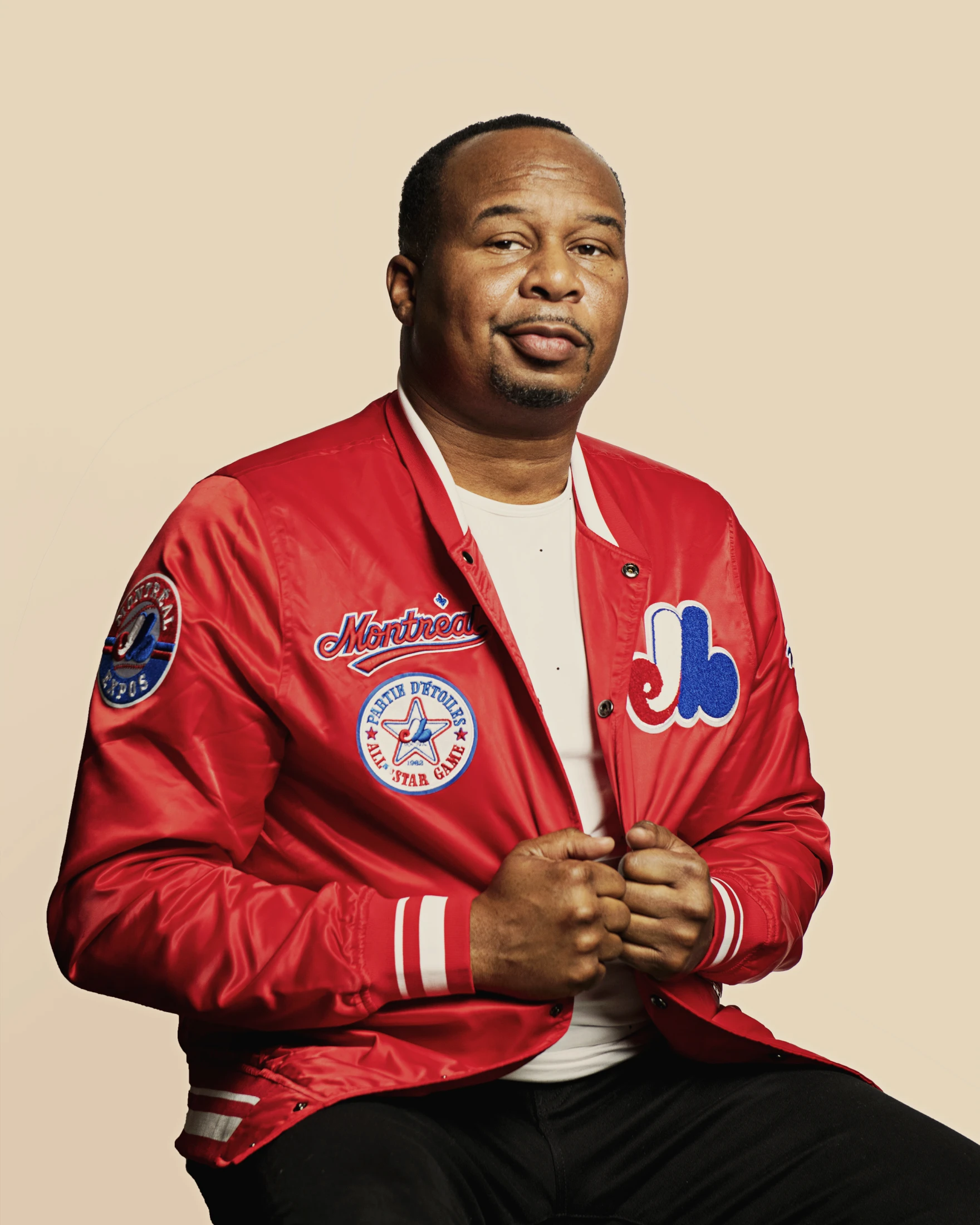 Roy Wood Jr. wearing a bright red Montreal Expos jacket against a light beige background.